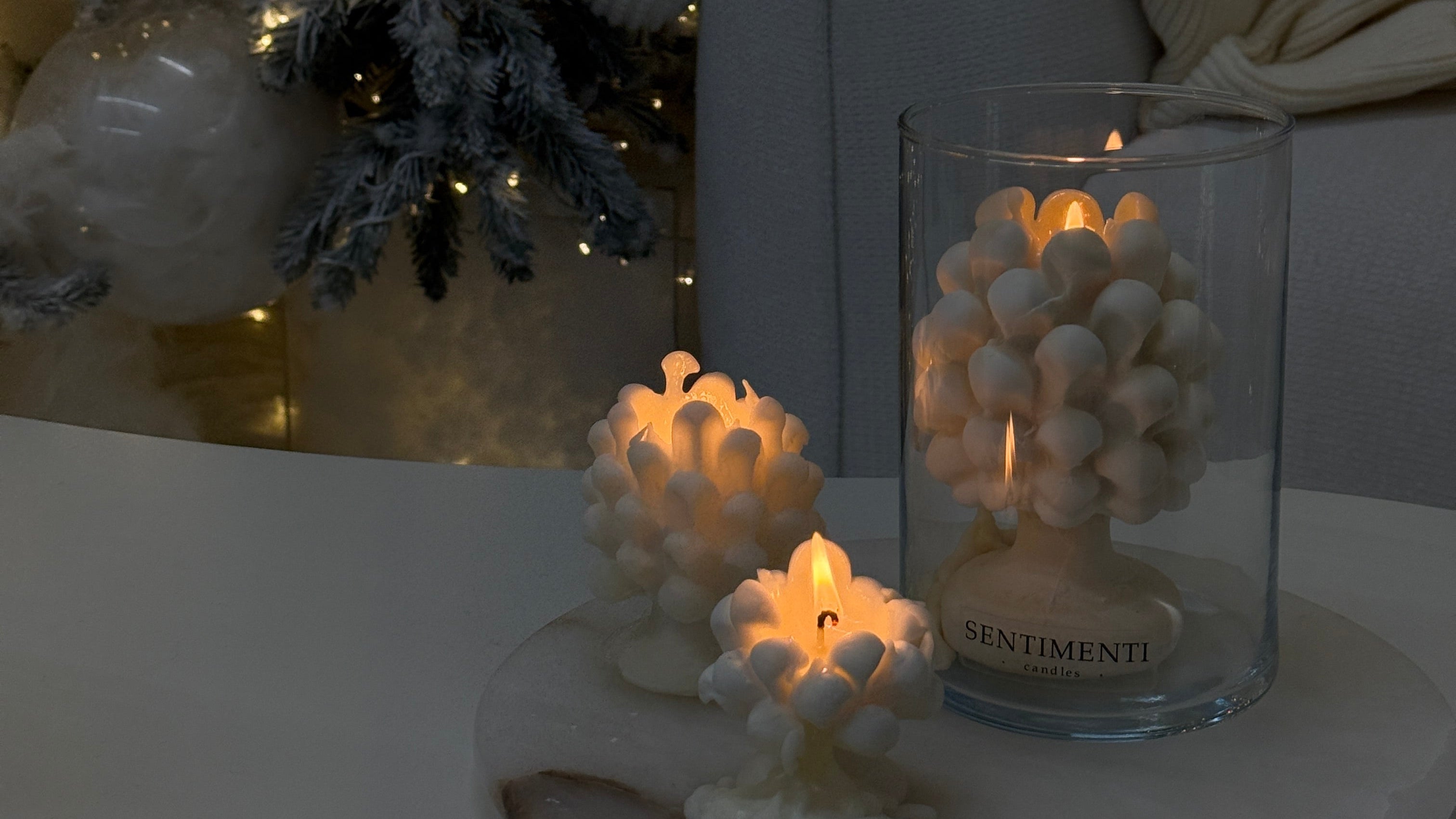 Decorative scene with a Christmas tree, candles, and a glass vase on a white surface.